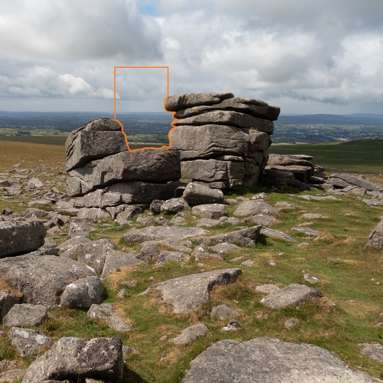 The view across the valley is partially framed by a weathered outcrop of stones.